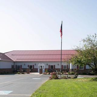 A building with a red roof and an American flag on a pole, surrounded by a driveway and lawn.