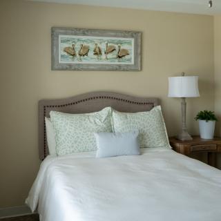 A cozy bedroom with a neatly made bed, decorative pillows, and a framed picture above the headboard.