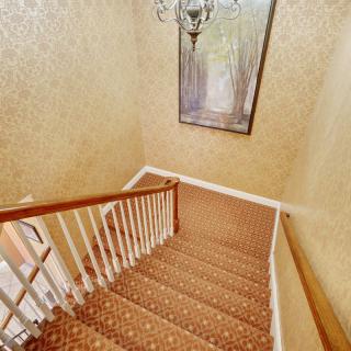 A carpeted staircase with a wooden railing, adorned by a chandelier and a large painting on the wall.