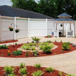 A beautifully landscaped garden with a central gazebo, surrounded by mulched flower beds and a white fence.