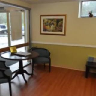 A cozy waiting area with a small table and chairs, featuring a painting on the wall and wooden flooring.