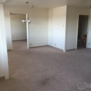 A spacious and empty living area with neutral-colored walls and a carpeted floor.