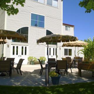 Sunny patio with outdoor seating and umbrellas in front of a building.