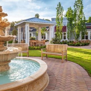 A serene outdoor space featuring a beautifully designed fountain and inviting benches surrounded by lush greenery.