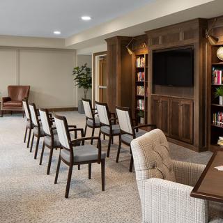 A cozy meeting room with chairs arranged in rows, a large bookshelf, and a television mounted on the wall.