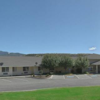A one-story building with a parking lot, surrounded by grass and mountains under a clear sky.