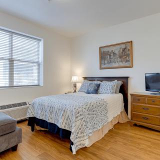 A well-lit bedroom with a cozy bed, artwork on the wall, and a television.