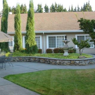 A serene garden patio with a central fountain, surrounded by neatly trimmed trees and a well-maintained lawn.