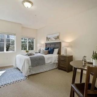 A cozy bedroom with a neatly made bed, side tables, and natural light streaming through the windows.