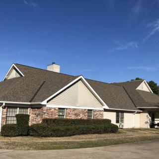A suburban residential house with a pitched roof and brick exterior under a clear blue sky.
