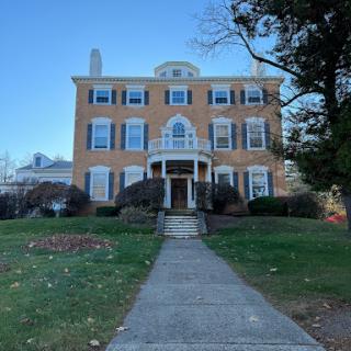 A charming brick residential building with a grand entrance, surrounded by manicured lawns.