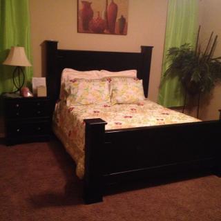 A cozy bedroom with a dark wooden bed, nightstand with a lamp, and green curtains.
