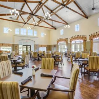 A spacious dining room with high ceilings, featuring multiple tables and striped chairs.