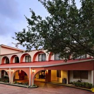 Exterior view of a hotel building with arches and surrounding trees in the evening.