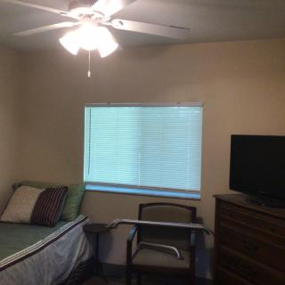 A small bedroom with a single bed, ceiling fan, and TV.