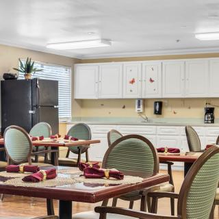 A modern dining area with neatly arranged tables and chairs, featuring a kitchenette in the background.