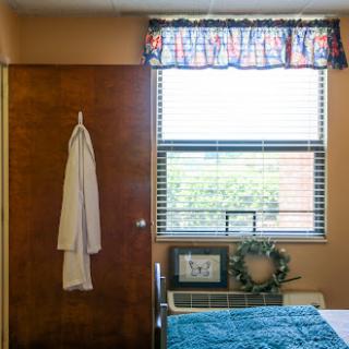 A cozy bedroom featuring a door, window with colorful curtains, and a neatly made bed.