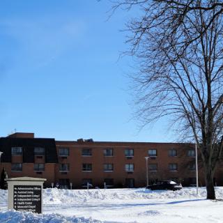 A winter scene featuring a brick building surrounded by snow and a bare tree under a clear blue sky.