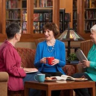 Three people engaged in a lively conversation over coffee in a library setting.