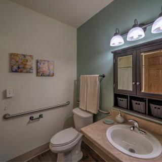 A well-lit bathroom with a toilet, sink, mirror, and decorative artwork on the walls.