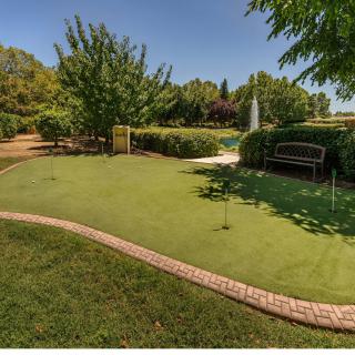 A well-maintained outdoor putting green surrounded by lush landscaping and a bench.