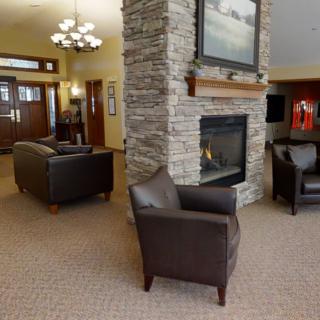 A cozy living room with a stone fireplace, leather chairs, and carpeted flooring.