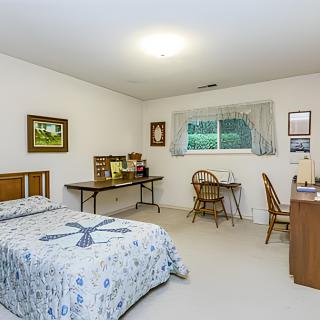 A cozy bedroom featuring a bed with patterned bedding, a desk with a chair, and artwork on the walls.