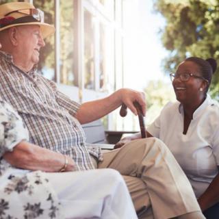 An elderly man enjoying a conversation with a caregiver outdoors.