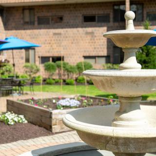 A peaceful garden patio with a stone fountain and outdoor seating under blue umbrellas.