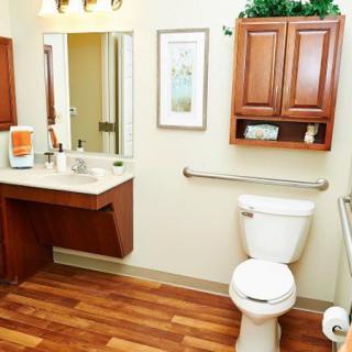 A clean and modern bathroom with wooden flooring, featuring a toilet, sink with mirror, and storage cabinets.