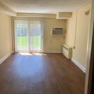An empty room with hardwood floors and a sliding glass door letting in natural light.