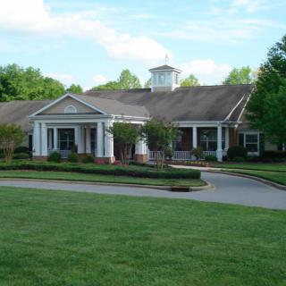 A large building with a prominent entrance surrounded by greenery and a well-kept lawn under a clear sky.