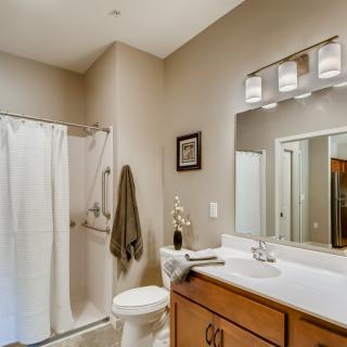 A modern bathroom featuring a sink and mirror, with a shower and toilet adjacent to the countertop.