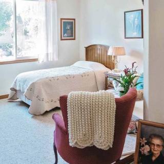 A cozy bedroom with a bed, chair, and lamp near a window.