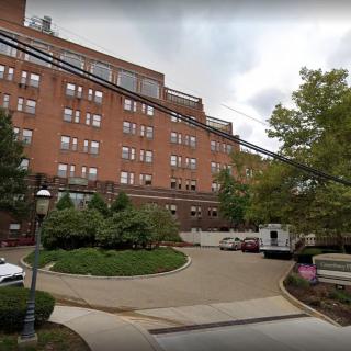 A red brick residential building with trees and cars in front.