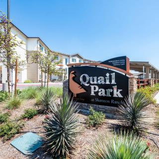 Entrance sign for Quail Park surrounded by landscaped greenery and residential buildings.