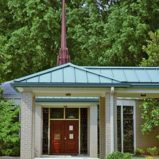 A small church building with a steeple surrounded by trees.