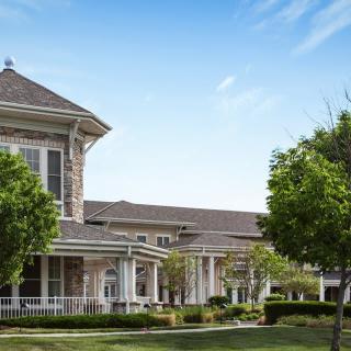 A large residential house with a front porch, surrounded by trees and under a clear blue sky.