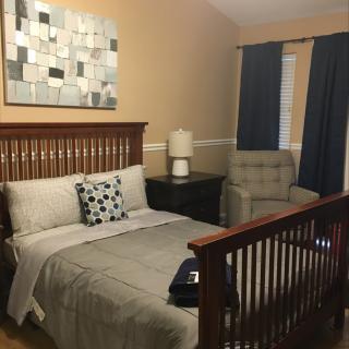 A cozy bedroom featuring a comfy bed, crib, and stylish decor.