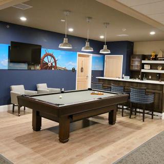 A modern game room featuring a pool table, bar seating, and a large TV.