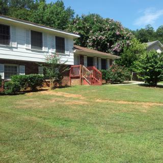 A suburban house with a well-maintained lawn and surrounded by trees on a sunny day.