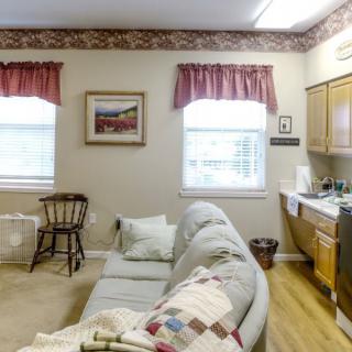 A cozy living room with a sofa and kitchenette, adorned with traditional decor and red curtains.