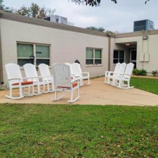A patio area with white chairs arranged outside a building on a grassy lawn.