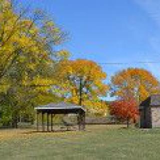 A scenic autumn landscape with trees showcasing vibrant fall colors, a small pavilion, and an open field.