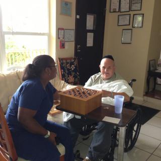 A caregiver and an elderly person enjoying a board game together in a cozy room.