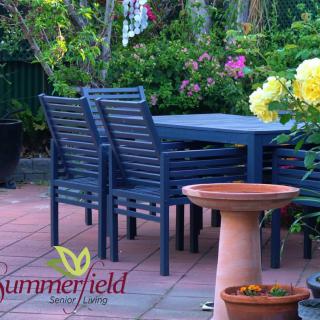A serene garden patio with blue furniture surrounded by lush greenery and blooming flowers.