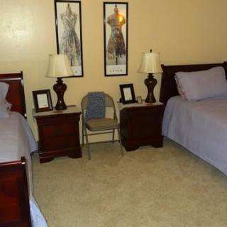 A cozy bedroom featuring two twin beds, nightstands with lamps, artwork on the wall, and a chair between the beds.