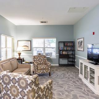 A cozy living room with patterned armchairs, a sofa, bookshelf, and TV.
