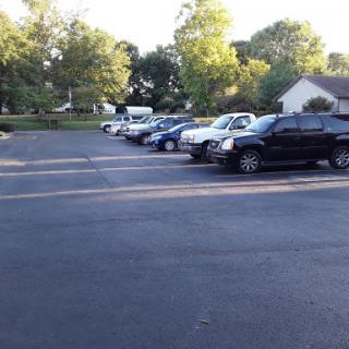 A view of a parking lot filled with various cars surrounded by trees on a sunny day.