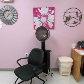 A hair salon interior featuring a dryer chair against a pink wall with decorative artwork.